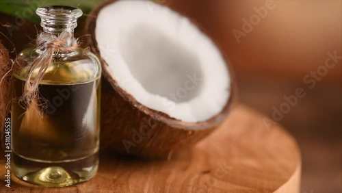 Coconut oil in a bottle with coconuts and green palm tree leaf rotated over brown background. Tropical Coco nut closeup. Healthy Food, skin care concept. Vegan food. 4K UHD video.  photo