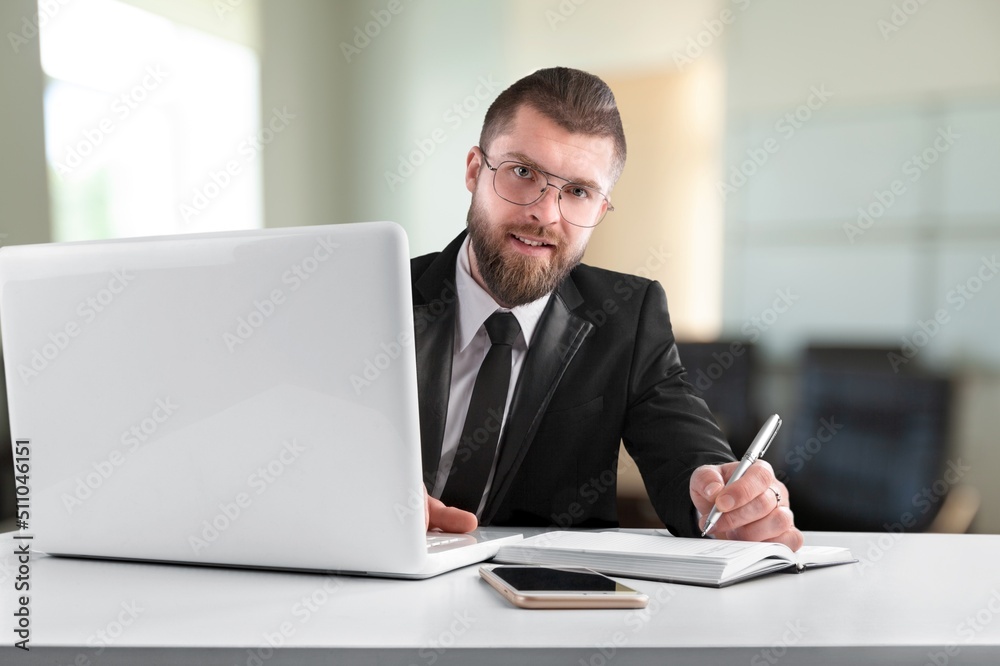 Smiling young businessman sitting at worktable at modern office, Smiling young businessman sitting at worktable at modern office,