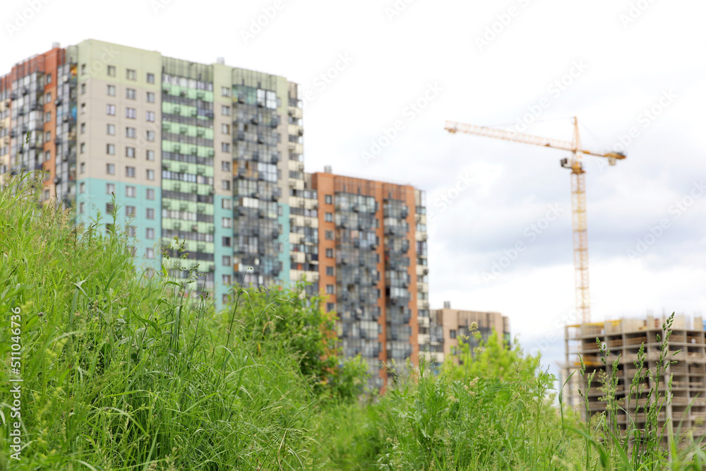 View to new residential buildings and construction crane from summer meadow with green grass. Concept of real estate in ecologically clean area View to new residential buildings and construction crane from summer meadow with green grass. Concept of real estate in ecologically clean area