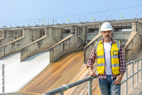A dam engineering doing his checking routine. He is wearing a white hard hat and yellow transparent vest. He is standing by the rail by the dam. © Attayoot