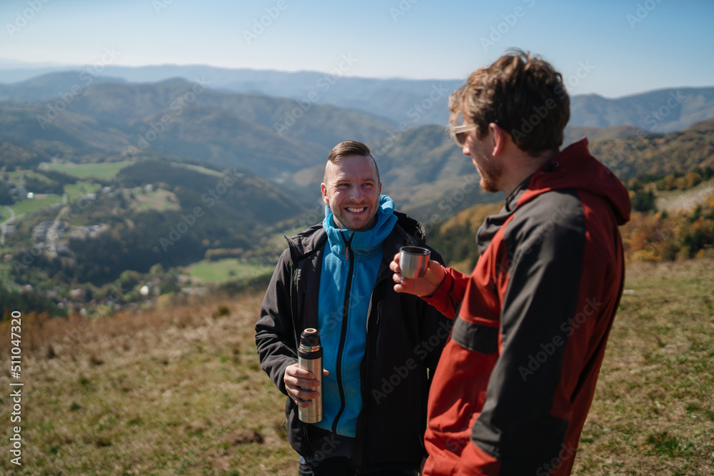 Two paragliders men standing on the top of mountain and drinking tea.