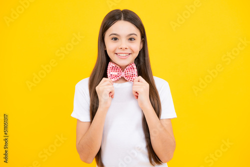 Teenager portrait of smiling girl child in t-shirt with bowtie isolated on yellow background. © Olena