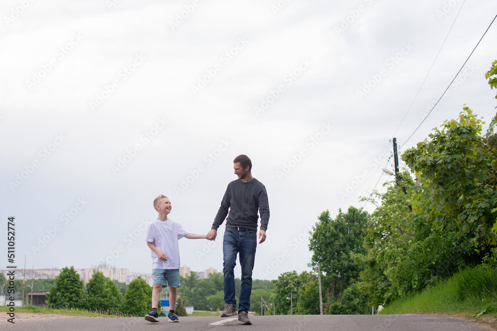 A father walks with his son on the road. The child is indulging A father walks with his son on the road. The child is indulging