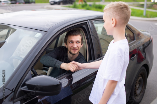 A cute child shakes hands with a happy father . Dad is sitting in the car and smiling