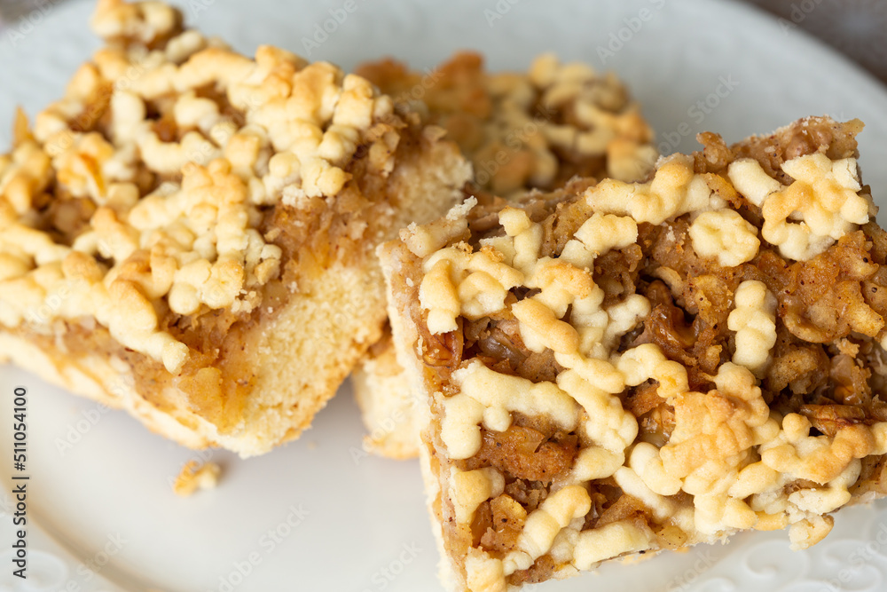 Square slice apple pie with walnuts on white porcelain plate in selective focus. Breakfast or after-dinner dessert concept. Square slice apple pie with walnuts on white porcelain plate in selective focus. Breakfast or after-dinner dessert concept.