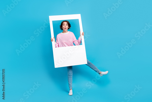 Full size photo of impressed pretty girl fooling around with big white snapshot frame isolated on blue color background