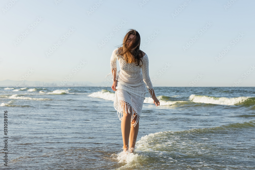 Brunette woman in dress standing in sea water. Brunette woman in dress standing in sea water.