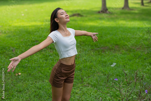 Portrait photo of a young beautiful asian female lady in white top embracing the breeze wind relaxingly and chillingly in a public park © asean studio