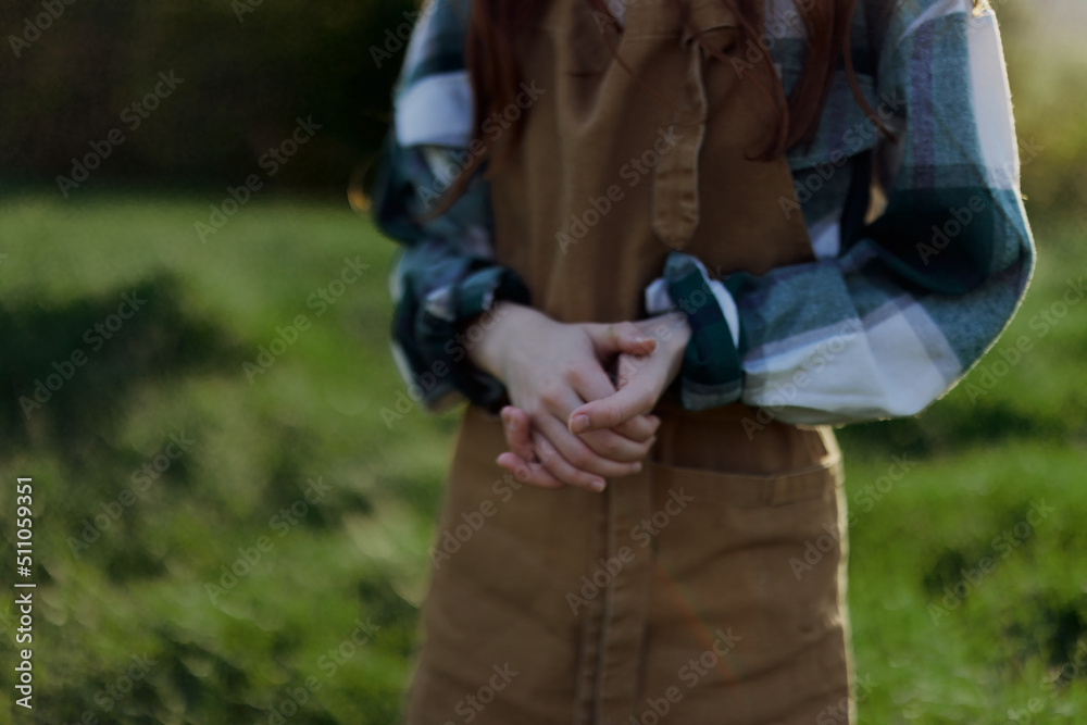 Close-up of a woman in a gardener's work apron against the green, fresh summer grass outdoors showing her hands