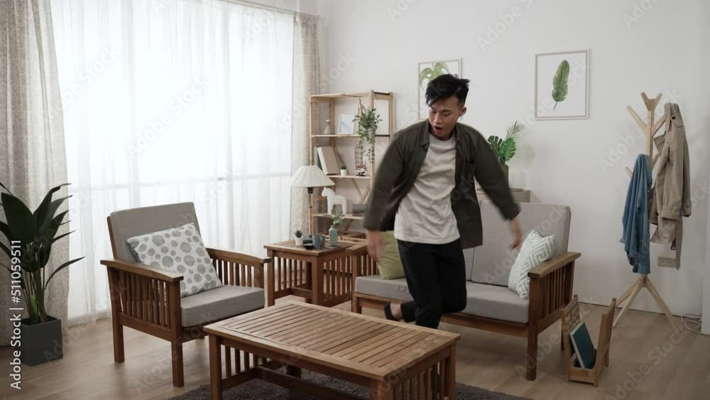 slow motion of an active asian male enjoying pop dancing in the living room at home with wood furniture during daytime. slow motion of an active asian male enjoying pop dancing in the living room at home with wood furniture during daytime.