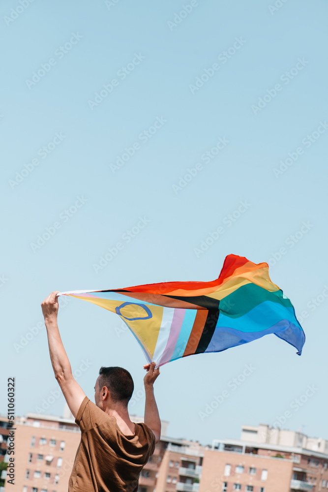 waves a progress pride flag above his head - obrazy, fototapety, plakaty 