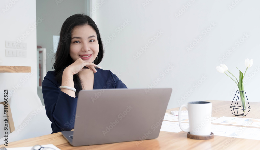 Charming Asian woman working at the office using a laptop Looking at the camera. Charming Asian woman working at the office using a laptop Looking at the camera.
