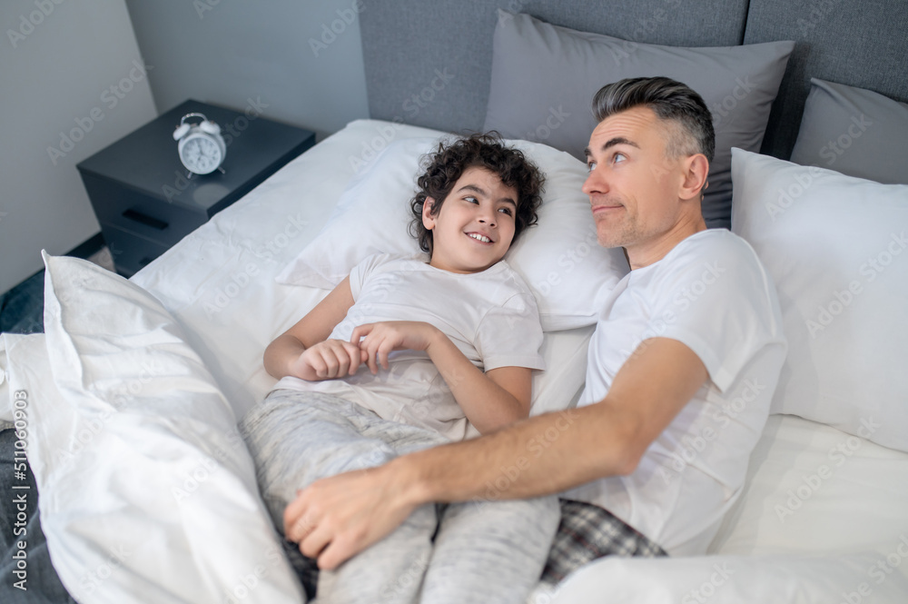 Fototapeta premium Father and son talking in bed in the morning and looking cheerful