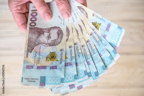 Money of Ukraine. Stack of ukrainian hryvnia banknotes in hands on wooden table. Hryvnia 1000 uah
