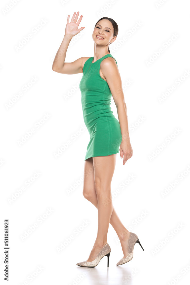 Side view of a a young happy woman in a short green dress waving hand on white background Side view of a a young happy woman in a short green dress waving hand on white background