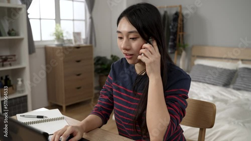 Asian young woman using computer is talking in happy surprise after receiving a notification call about getting great job interview opportunity at home.