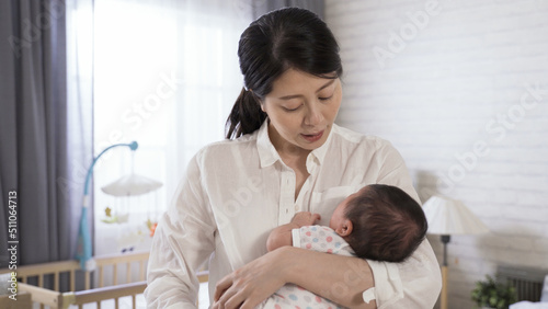 asian first time mom is soothing her crying baby in her cuddle by talking with tenderness in the bedroom at home.