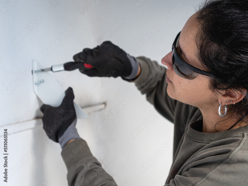 Fototapeta premium Latin woman with screwdriver attaching a piece of metal in the wall