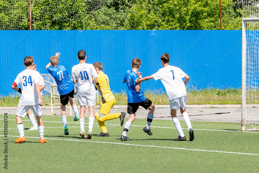 Obraz premium Children's football for boys aged 13-14. Active dynamic struggle for the ball between young men from the opposing teams on the green football field.