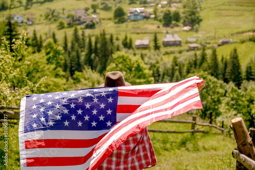 A young woman stands on a mountain and holds the US flag in her hands. American Independence Day celebration.