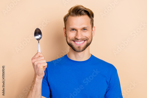 Portrait of satisfied young person hold demonstrate spoon toothy smile isolated on beige color background