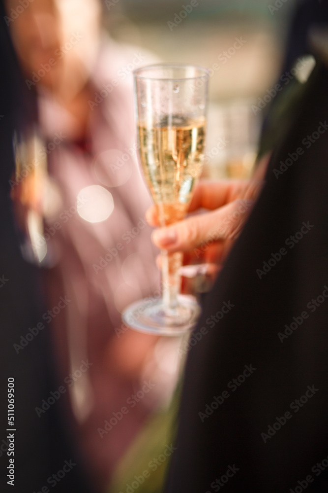 New Year's blurred festive background with a man's hand with a glass of champagne and bokeh from fireworks. wedding champagne party. the groom in a suit holds a glass of champagne in his hand. blurry