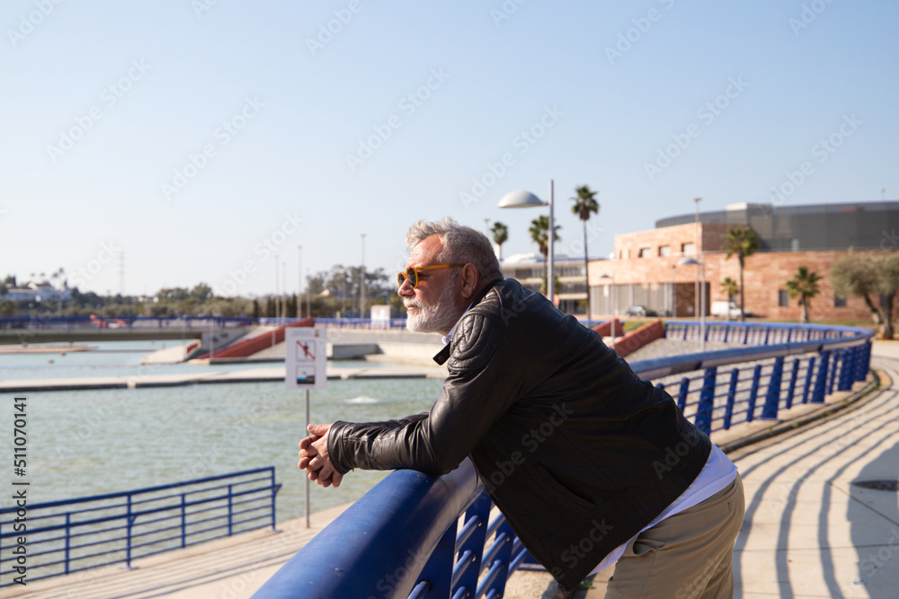 handsome mature man with beard and grey hair is walking in the park. The man is dressed in beige trousers, white shirt and leather jacket. Old age concept handsome mature man with beard and grey hair is walking in the park. The man is dressed in beige trousers, white shirt and leather jacket. Old age concept