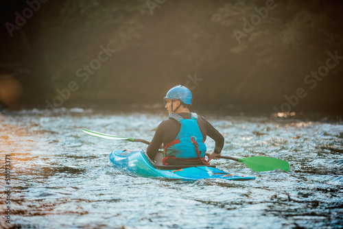 Fototapeta Naklejka Na Ścianę i Meble -  Young teenager cruising down whitewater rapids in a blue kayak, beautiful river nature on a sunny summer day, handheld shot.