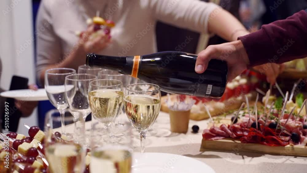 Waiter pouring glasses with champagne on catering service on banquet table with canape snacks in restaurant or hotel. Food set on birthday, wedding celebration or business conference event venue.