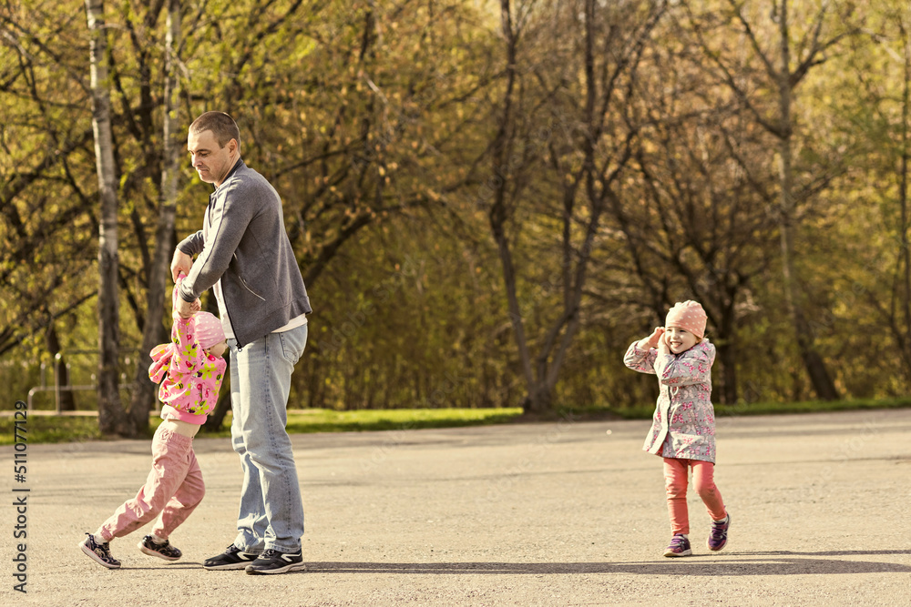 Fototapeta premium Dad plays with his daughters in the park. Twirling a girl around. Family