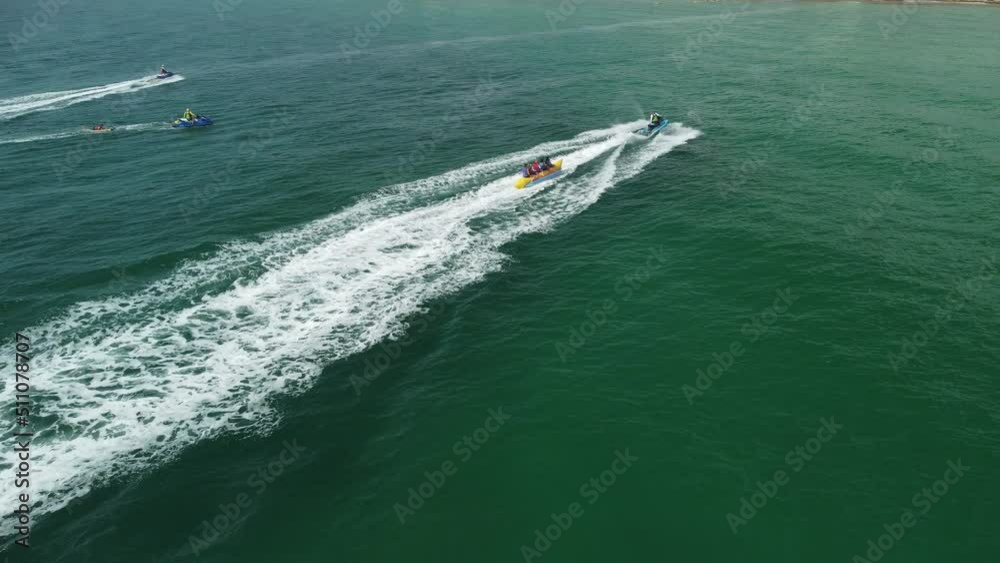 Aerial view of a jet ski pulling thrill seekers on an inflatable banana boat ride on a sunny South Florida day at the beach. Aerial view of a jet ski pulling thrill seekers on an inflatable banana boat ride on a sunny South Florida day at the beach.