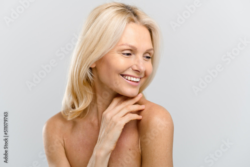 Mature lady looking away and smiling. Portrait of fresh and gorgeous senior woman with healthy skin and blonde hair, posing with naked shoulders isolated on white background photo