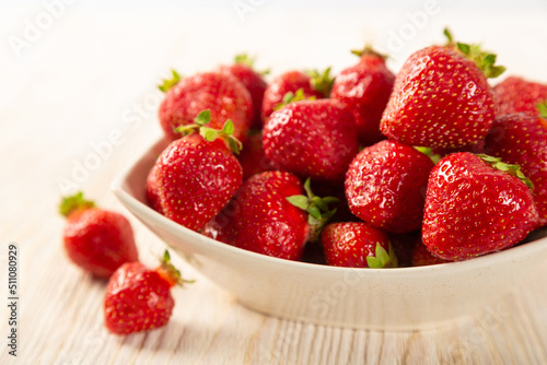Red strawberry in a white plate on a wooden background