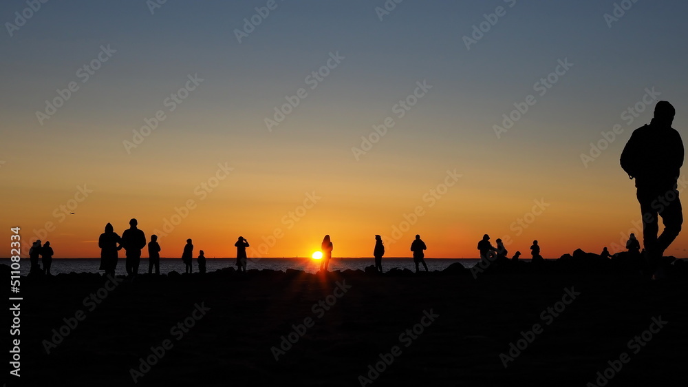 Romantic landscape. Silhouettes of people seeing off the sun on the seashore against the backdrop of a colorful sunset.