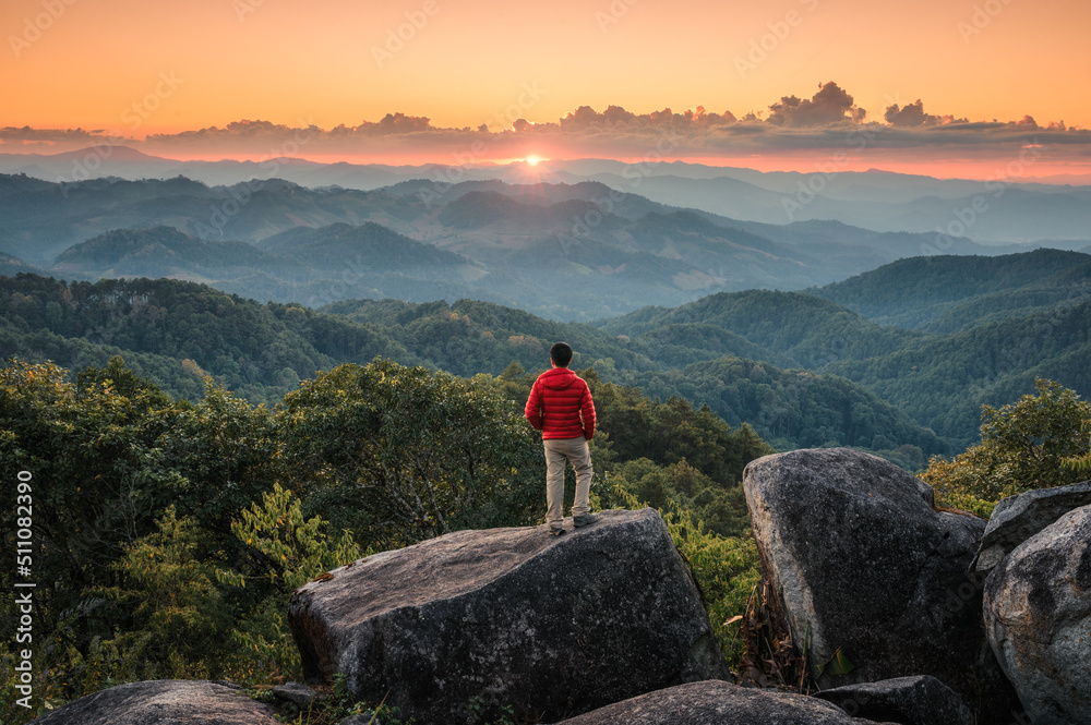 Hiker man standing on top of mountain enjoying the beautiful sunset in tropical rainforest at national park