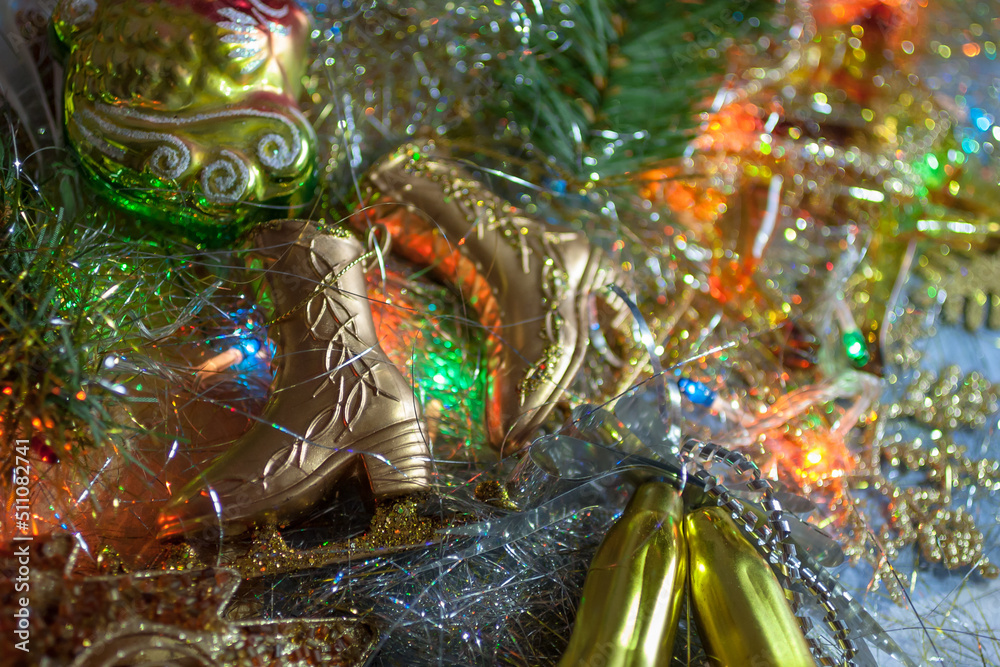 Closeup of the golden skates with the fir branch on the silver tinsel and the colorful garland. Top view. New year, Christmas background Closeup of the golden skates with the fir branch on the silver tinsel and the colorful garland. Top view. New year, Christmas background