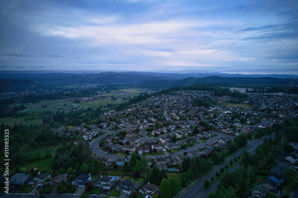Obraz premium An aerial view of a residential community in a valley surrounded by forests of evergreen trees taken during sunrise.
