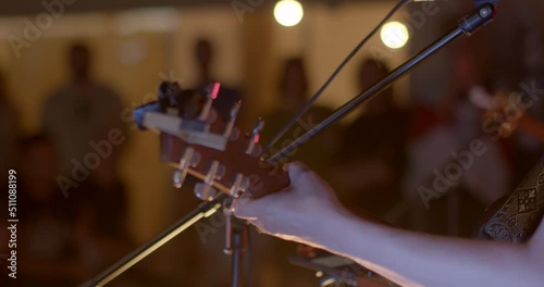 Close-up of a musician's hand and guitar neck. He makes chords in music. The pegs hold the strings of a musical instrument. In the background, the audience in bokeh. photo