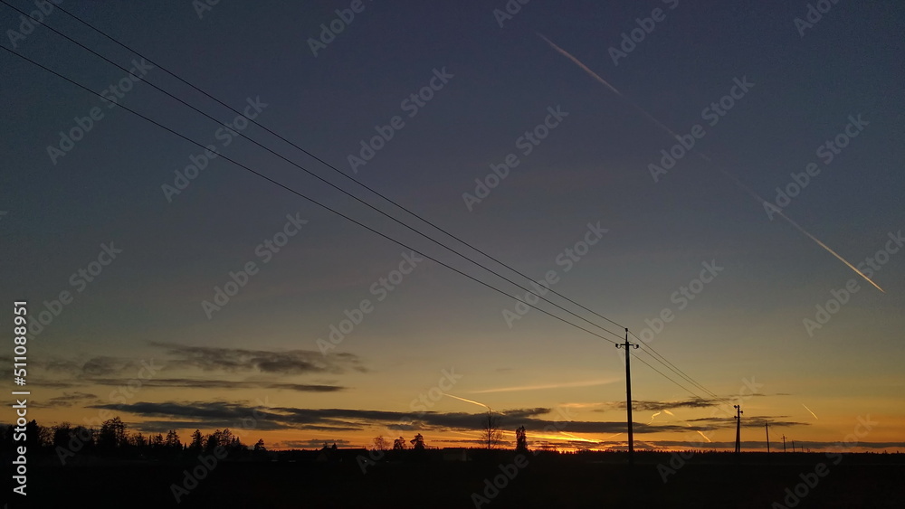 Rural landscape. Silhouettes of power lines and trees against the backdrop of a colorful sunset.