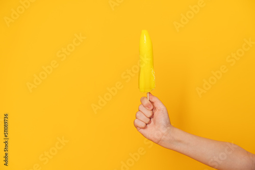 Child's hand holding ice cream on stick in the shape of rocket against yellow background.