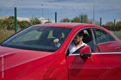 Handsome young man with beard  sunglasses and white shirt  inside his red sports car. Concept beauty  fashion  trend  luxury  motor  sports  winner.