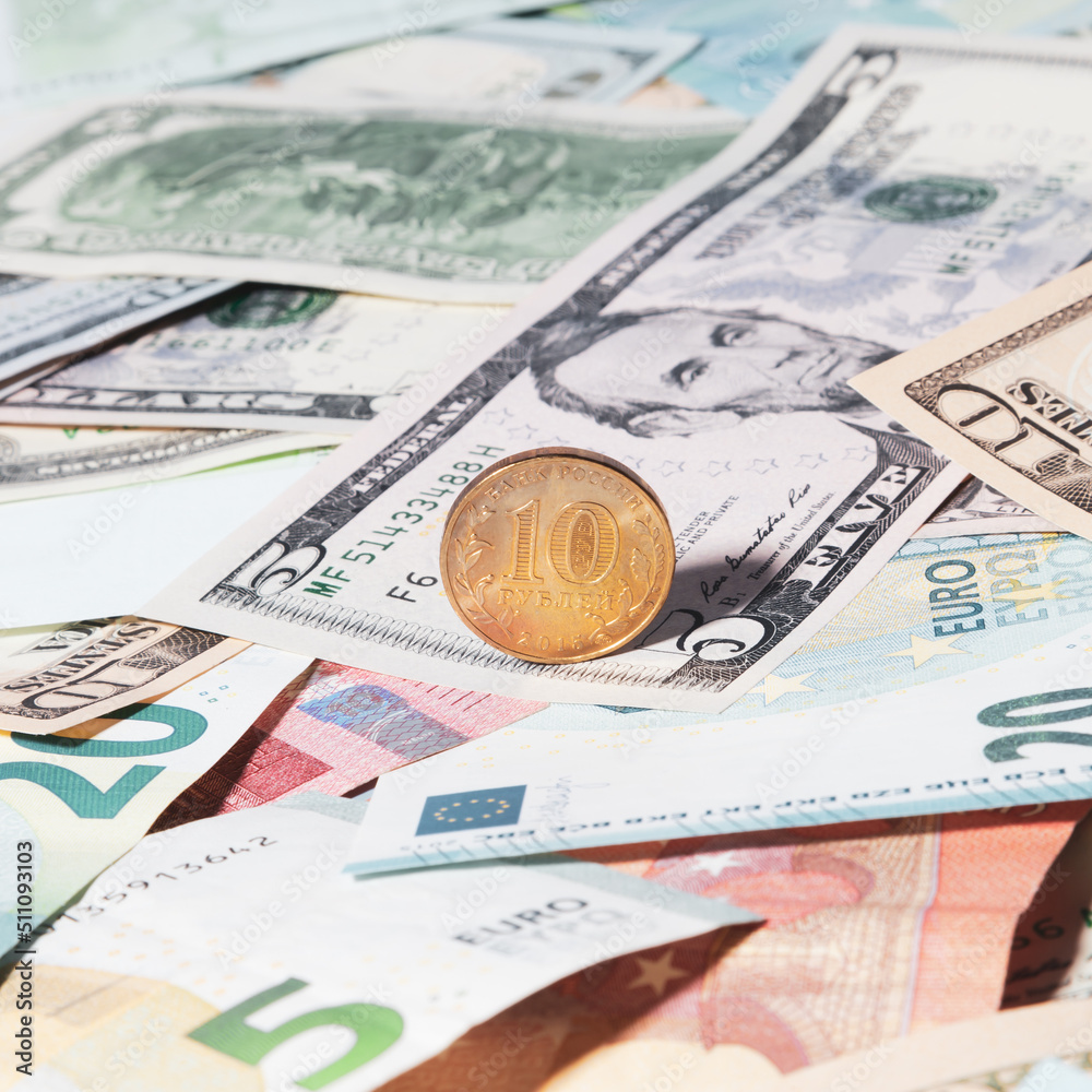 A gold-colored coin with a denomination of 10 Russian rubles lies on top of USA and European paper money of different denominations - USD, EUR. View from above. Russian ruble coins. A gold-colored coin with a denomination of 10 Russian rubles lies on top of USA and European paper money of different denominations - USD, EUR. View from above. Russian ruble coins.