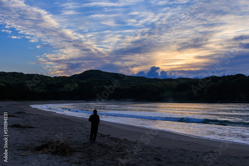 伊豆の弓ヶ浜の美しい朝日の中で砂浜に立つ男性
