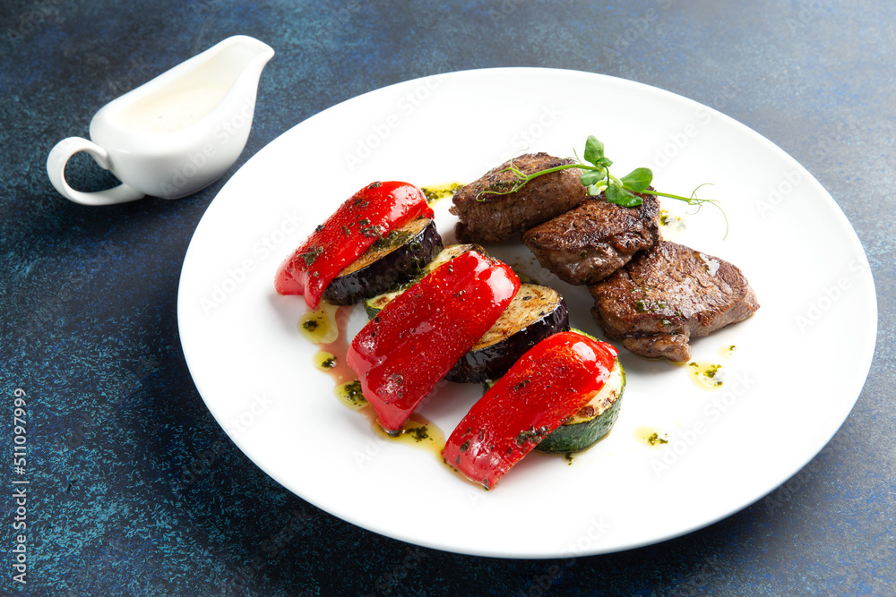 Beef medallions and grilled vegetables. On a gray background. Beef medallions and grilled vegetables. On a gray background.