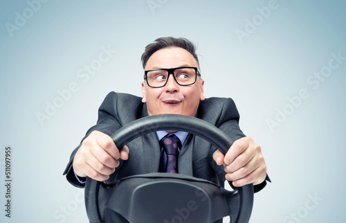 Fotografie, Tablou Portrait of a comical businessman in a dark suit and glasses holding a car steer