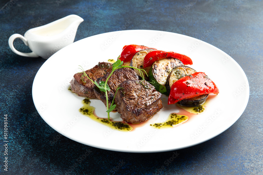 Beef medallions and grilled vegetables. On a gray background. Beef medallions and grilled vegetables. On a gray background.