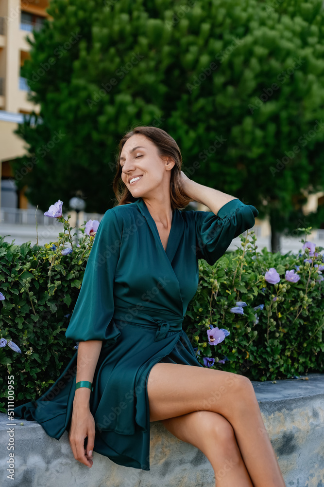 A smiling, sophisticated girl in a turquoise light dress walks in a well-kept green park. It's a hot summer in a tropical country. A smiling, sophisticated girl in a turquoise light dress walks in a well-kept green park. It's a hot summer in a tropical country.