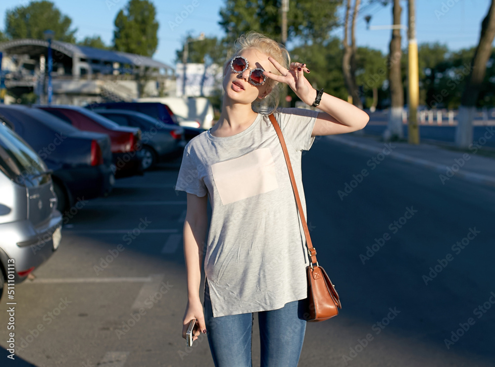 Fototapeta premium Attractive cheerful girl walking in urban city, wear sunglasses, show v-sign.