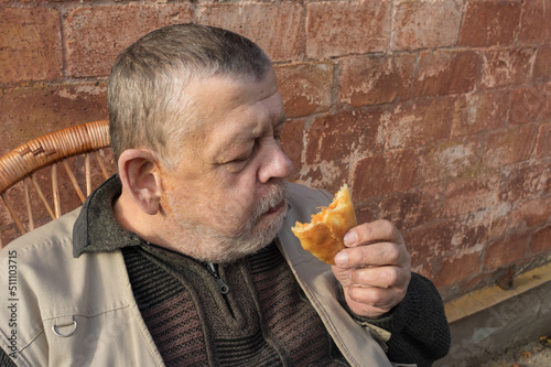 Portrait of Ukainian senior Sitting agaist brick wall and eating patty filled with fried cabbage photo
