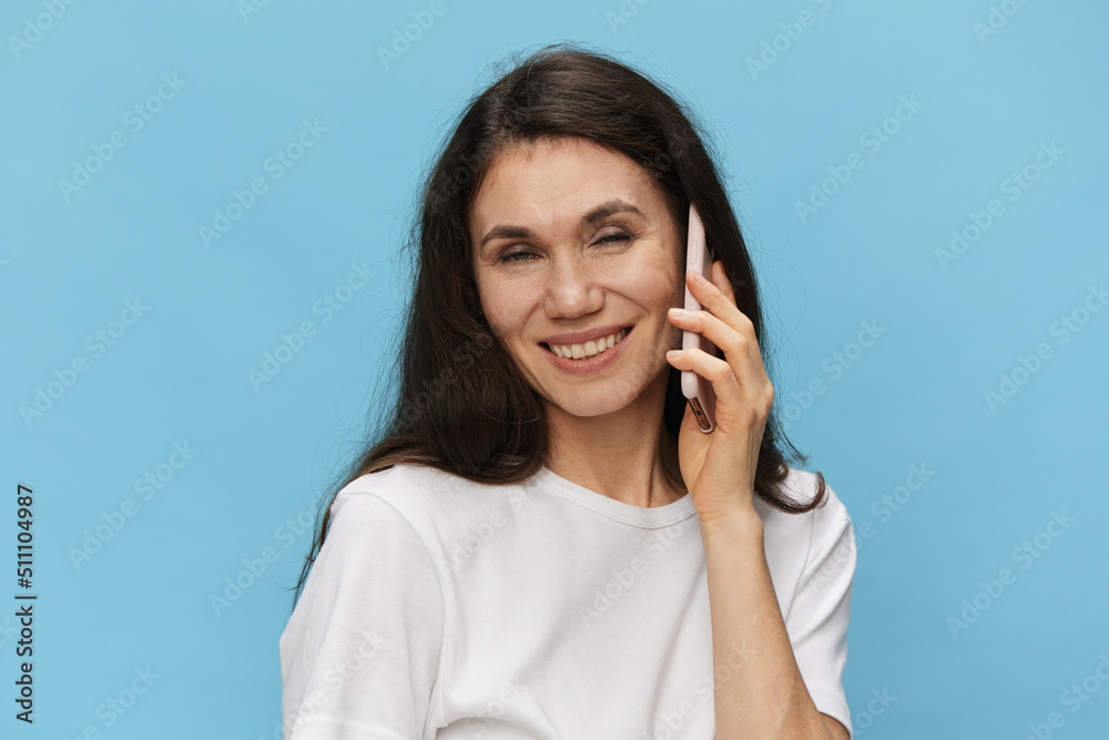 woman talking on the phone pleasantly closing her eyes and smiling broadly while standing on a light blue background with empty space to insert an advertising layout woman talking on the phone pleasantly closing her eyes and smiling broadly while standing on a light blue background with empty space to insert an advertising layout